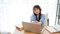 A cute young Asian girl is feeling tired, stretching her arms while studying online at home