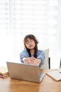 A cute young Asian girl is feeling tired, stretching her arms while studying online at home