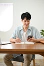 Cute young Asian male college student using his smartphone while doing homework Royalty Free Stock Photo