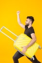 Cute young bearded hipster man holding a heavy yellow suitcase on a yellow background. Concept of heavy load for Royalty Free Stock Photo