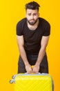 Cute young bearded hipster man holding a heavy yellow suitcase on a yellow background. Concept of heavy load for Royalty Free Stock Photo