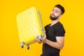 Cute young bearded hipster man holding a heavy yellow suitcase on a yellow background. Concept of heavy load for Royalty Free Stock Photo