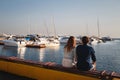 Cute young beautiful couple sitting and hugging together at pier at port, hipsters. Back view