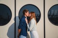 Cute young beautiful hipster couple kissing at port, on the white wall with big portholes background