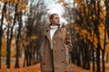 Cute young blond woman with a stylish warm coat in a vintage white sweater in posing in an autumn park. Pretty elegant girl enjoys Royalty Free Stock Photo