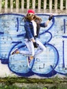 Cute young blonde teenager girl in a baseball cap and jeans shirt jumping against a stone wall background. Hip hop, Royalty Free Stock Photo