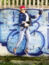 Cute young blonde teenager girl in a baseball cap and jeans shirt jumping against a stone wall background. Hip hop, Royalty Free Stock Photo