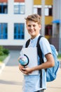 Cute, young boy in blue shirt with backpack stands in front of his school. Education, Back to school Royalty Free Stock Photo