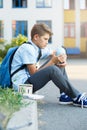 Cute, young boy in blue shirt with backpack stands in front of his school. Education, Back to school Royalty Free Stock Photo