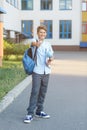 Cute, young boy in blue shirt with backpack stands in front of his school. Education, Back to school Royalty Free Stock Photo