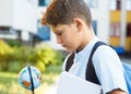 Cute, young boy in blue shirt with backpack stands in front of his school. Education, Back to school Royalty Free Stock Photo