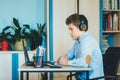 Cute young boy in blue shirt sitting behind desk in his room next to laptop and study. Teenager in earphones makes homework,