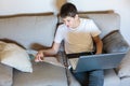 Cute young boy in glasses and white t shirt sitting on the couch in the living room with laptop and study. Homeschooling, Royalty Free Stock Photo