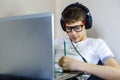 Cute young boy in glasses and white t shirt sitting on the couch in the living room with laptop and study. Homeschooling,