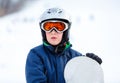 Cute young boy in gray helmet and orange googles, in blue jacket holds snowboard on white snow background. winter sport Royalty Free Stock Photo