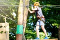 Cute young boy in helmet with climbing equipment in the rope amusement park. Summer camp, holidays