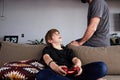 Cute young boy playing video game console seated on a sofa while his father standing close in living room at home Royalty Free Stock Photo