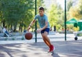 A cute young boy plays basketball on the street playground in summer. Teenager in a green t-shirt with orange basketball ball Royalty Free Stock Photo