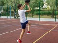 Cute young boy plays basketball on street playground in summer. Teenager in white t-shirt with orange basketball ball outside. Royalty Free Stock Photo