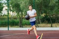 Cute young boy plays basketball on street playground in summer. Teenager in white t-shirt with orange basketball ball outside. Royalty Free Stock Photo