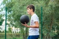 Cute young boy plays basketball on street playground in summer. Teenager in white t-shirt with orange basketball ball outside. Royalty Free Stock Photo