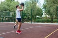 Cute young boy plays basketball on street playground in summer. Teenager in white t-shirt with orange basketball ball outside. Royalty Free Stock Photo