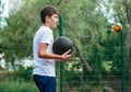 Cute young boy plays basketball on street playground in summer. Teenager in white t-shirt with orange basketball ball outside. Royalty Free Stock Photo