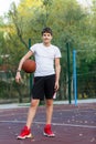 Cute young boy plays basketball on street playground in summer. Teenager in white t-shirt with orange basketball ball outside. Royalty Free Stock Photo