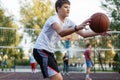 Cute young boy plays basketball on street playground in summer. Teenager in white t-shirt with orange basketball ball outside. Royalty Free Stock Photo