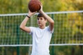 Cute young boy plays basketball on street playground in summer. Teenager in white t-shirt with orange basketball ball outside. Royalty Free Stock Photo