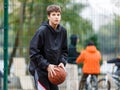 Cute young boy plays basketball on street playground. Teenager with orange basketball ball outside. Hobby, active lifestyle, sport Royalty Free Stock Photo