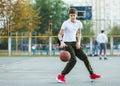 Cute young boy plays basketball on street playground. Teenager in white t shirt with orange basketball ball outside. Hobby, Royalty Free Stock Photo