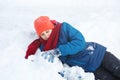Cute young boy in red hat blue jacket holds and plays with snow, has fun, smiles, makes snowman in winter park. Royalty Free Stock Photo