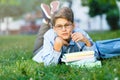 Cute, young boy in round glasses and blue shirt reads book on the grass in the park. Education, back to school Royalty Free Stock Photo