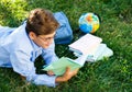 Cute, young boy in round glasses and blue shirt reads book while lying on the grass in the park. Education, back to school Royalty Free Stock Photo