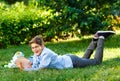 Cute, young boy in round glasses and blue shirt reads book while lying on the grass in the park. Education, back to school Royalty Free Stock Photo