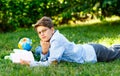 Cute, young boy in round glasses and blue shirt reads book while lying on the grass in the park. Education, back to school Royalty Free Stock Photo