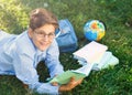 Cute, young boy in round glasses and blue shirt reads book while lying on the grass in the park. Education, back to school Royalty Free Stock Photo