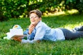 Cute, young boy in round glasses and blue shirt reads book while lying on the grass in the park. Education, back to school Royalty Free Stock Photo