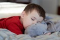 cute young boy taking a nap on the bed using his plush toy as a pillow