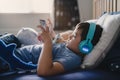 Cute young boy wear wireless headphone listening music while lying in bed, Happy kid playing game on tablet,Positive child in blue Royalty Free Stock Photo