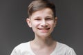 Cute young boy in white T-shirt posing in front of gray empty wall. Portrait of fashionable male child. Smiling boy posing, blank