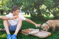 Cute, young boy in white t shirt sits on the grass and takes a slice of pizza in the summer park. Boy eats pizza