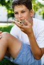 Cute, young boy in white t shirt sits on the grass and takes a slice of pizza in the summer park. Boy eats pizza