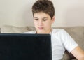 Cute young boy white t shirt sitting on the couch in the living room with laptop and study. Home education, self education Royalty Free Stock Photo