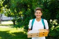 Cute, young boy in white t shirt stands on the grass and holds boxes with pizza in the summer park. Boy eats pizza Royalty Free Stock Photo