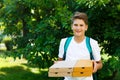 Cute, young boy in white t shirt stands on the grass and holds boxes with pizza in the summer park. Boy eats pizza Royalty Free Stock Photo