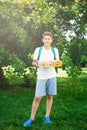 Cute, young boy in white t shirt stands on the grass and holds boxes with pizza in the summer park. Boy eats pizza Royalty Free Stock Photo