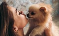 Cute young brunette girl kisses her Pomeranian spitz dog. The concept of home comfort and pet care Royalty Free Stock Photo