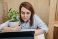 Cute young brunette woman in simple clothes shows SchefflerÃÂ° flower in white pot in her laptop. Online consultation about care of